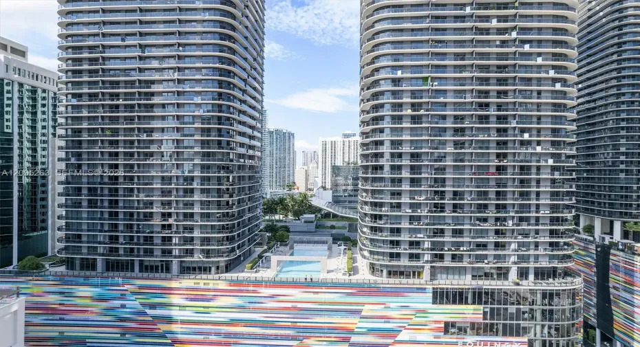 High-rise residential towers featuring wrap-around glass balconies, exterior multi-colored mural facade, and outdoor swimming pool