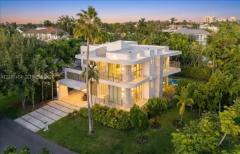 Multi-level modern exterior featuring stone cladding, expansive floor-to-ceiling glass windows, multiple wrap-around balconies, and a concrete paver driveway