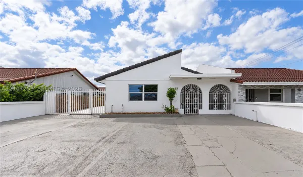 Asymmetric roofline, decorative arched entryways, metal security grilles, and a concrete driveway enclosed by perimeter walls