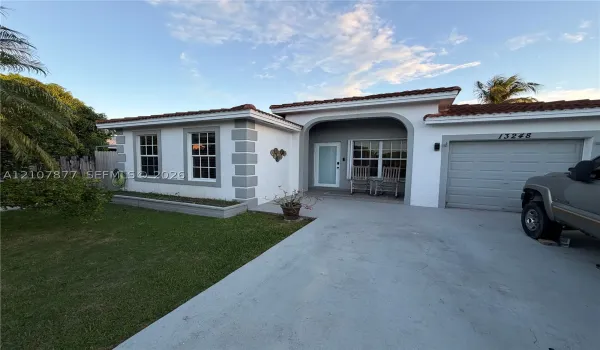 Single-story exterior featuring white stucco finish, contrasting grey quoins, arched covered entryway, multi-pane windows, and a concrete driveway