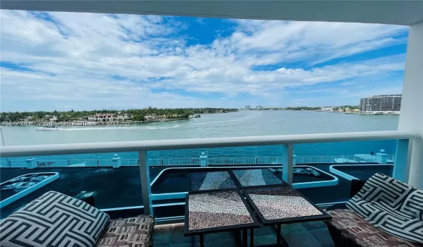 Private balcony featuring a glass-panel railing and stone-tile flooring overlooking an expansive water expanse
