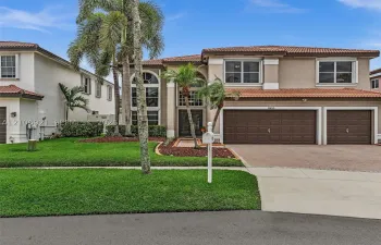 Stucco exterior featuring a multi-gabled tile roof, arched entryway, brick-patterned driveway, and a three-car garage