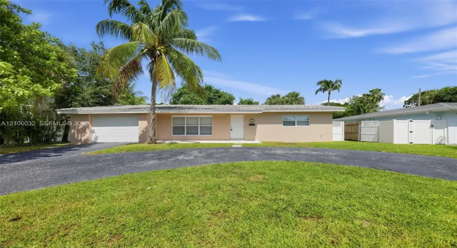Single-story residence featuring a stucco exterior, concrete tile roof, attached one-car garage, curved asphalt driveway, and perimeter white vinyl fencing