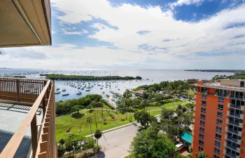 Elevated outdoor balcony with metal railing, overlooking a coastal expanse, harbor, and landscaped green space