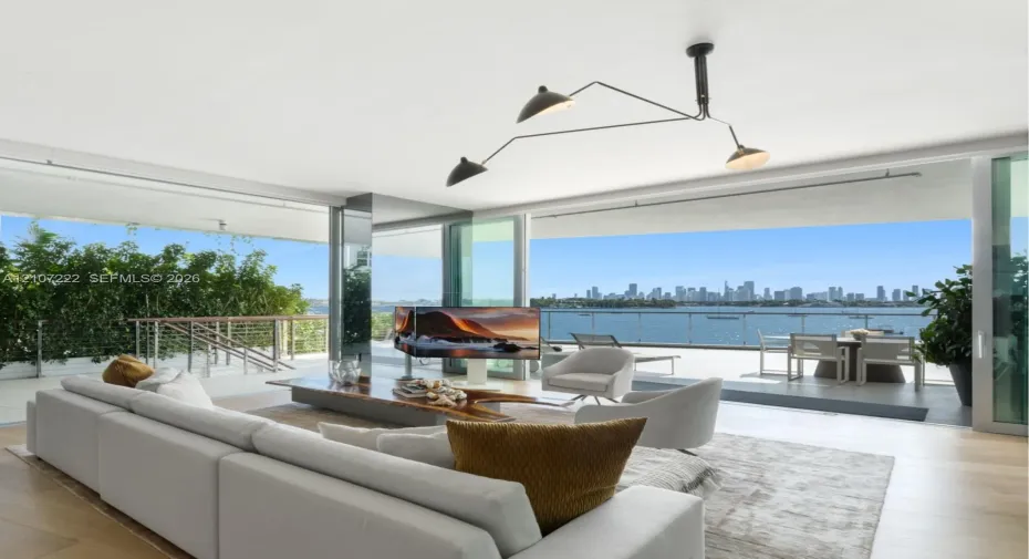 Open-concept interior featuring floor-to-ceiling glass sliding doors, wood-finish flooring, architectural multi-arm pendant lighting, and a wrap-around balcony with metal​​‌​​​​‌​​‌‌​‌‌​​​‌‌​‌​‌​‌​​​‌​​ railing