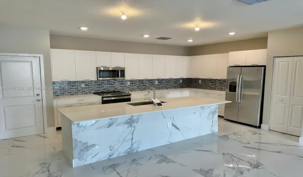 Kitchen featuring flat-panel white cabinetry, a center island with stone-finish waterfall edges, stainless steel appliances, and a glass tile backsplash