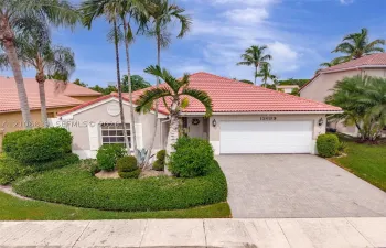 Single-story residence featuring a terracotta-tiled roof, paver driveway, attached two-car garage, and established landscaping with mature palm trees