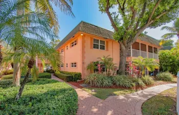 Two-story stucco exterior with a hip roof, multi-level screened-in balconies, paver walkways, and mature tropical landscaping