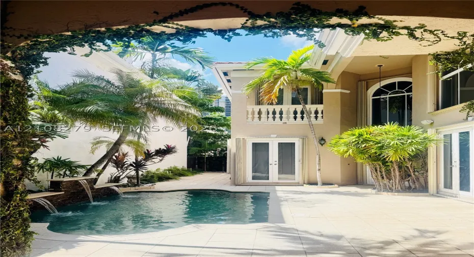 Private courtyard featuring a stone-tiled patio, a custom swimming pool with tiered waterfall features, a second-story balcony with decorative balustrades, and a two-story arched window