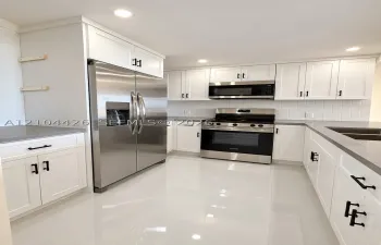 Kitchen featuring white shaker-style cabinetry, quartz countertops, stainless steel appliances, vertical tile backsplash, and polished tile flooring