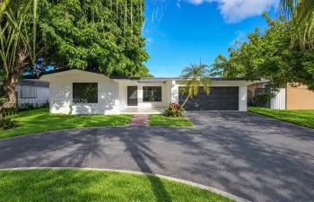 Single-story exterior featuring white stucco siding, a flat roofline, an integrated multi-panel garage door, and an asphalt driveway with a brick-paver walkway