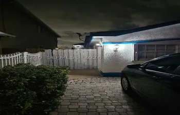 Textured stucco exterior featuring stone paver driveway, white privacy fencing, and exterior wall-mounted light fixtures