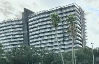 Modern high-rise exterior featuring a dark metallic facade, rhythmic rows of glass-railed balconies, and a stepped roofline