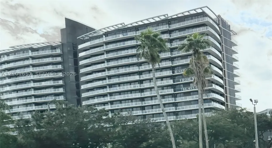 Modern high-rise exterior featuring a dark metallic facade, rhythmic rows of glass-railed balconies, and a stepped roofline