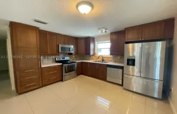 Kitchen featuring wood cabinetry, stainless steel appliances, tile backsplash, light-colored countertops, and large-format tile flooring