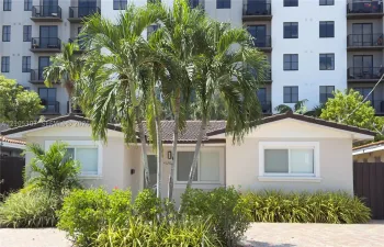 Single-story exterior featuring a light-colored stucco facade, tiled roof, paver driveway, and mature tropical landscaping
