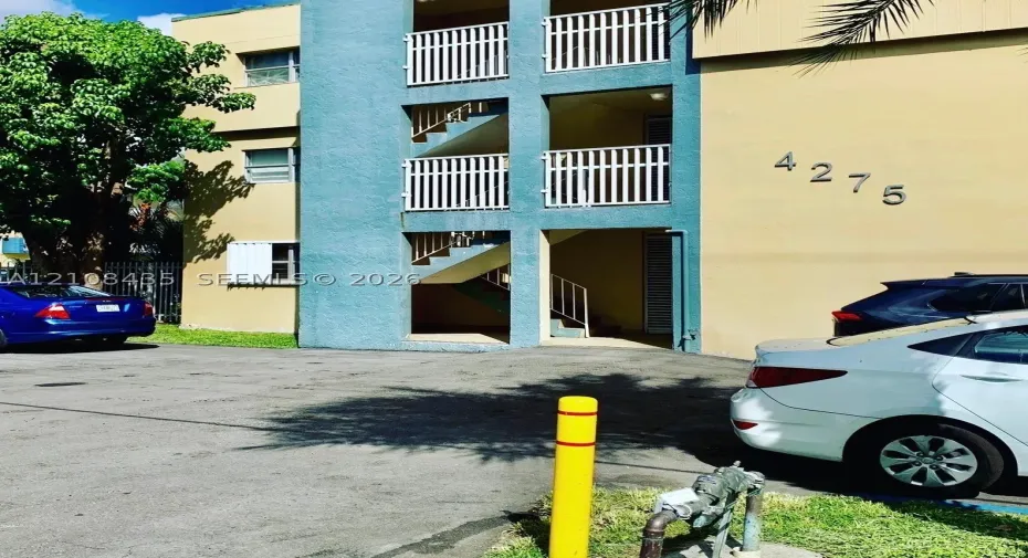 Multi-story exterior featuring a stucco facade, white metal balcony railings, and exterior staircases
