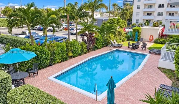 Rectangular swimming pool featuring a brick-paver deck, integrated entry steps, and metal handrails, bordered by mature palm trees and manicured privacy hedging