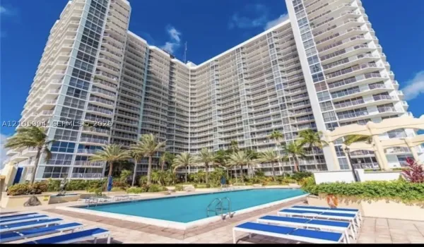High-rise building exterior featuring a multi-story facade with wraparound balconies, accompanied by an outdoor swimming pool, paved sun deck, and mature palm trees