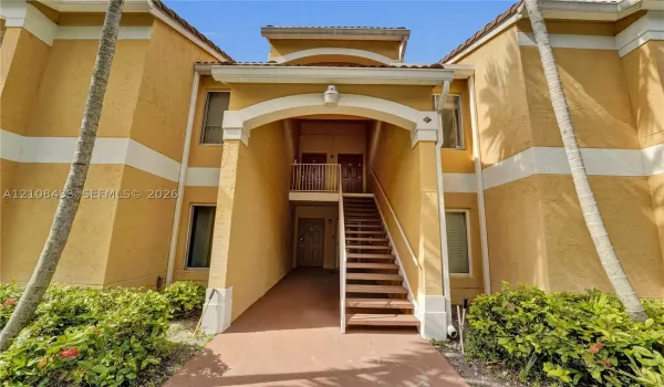 Stucco exterior featuring an arched entryway, decorative trim, tiled roofline, and exterior staircase