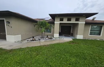 Stucco exterior with decorative columns, integrated solar panels, recessed entry lighting, and low-maintenance rock garden landscaping