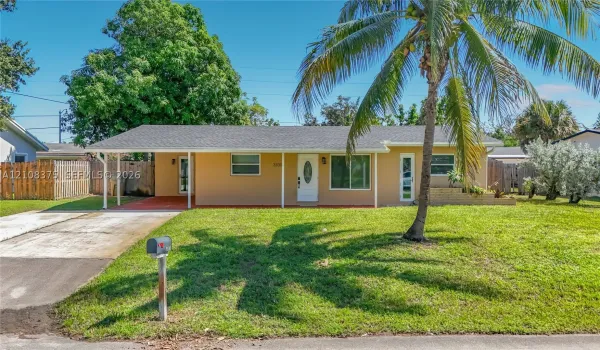 Single-story exterior featuring a concrete driveway, attached carport, manicured lawn, and mature palm tree