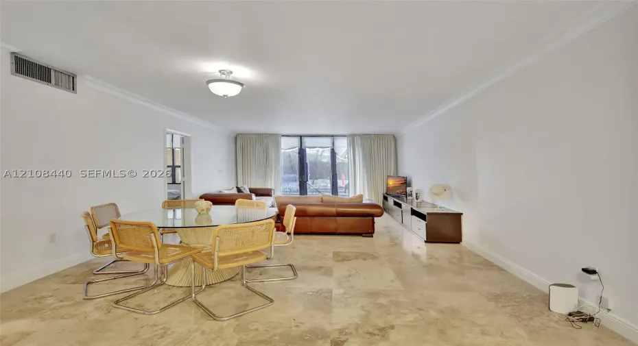 Open-concept interior featuring large-format stone flooring, crown molding, and floor-to-ceiling glass panel doors