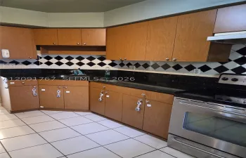 Kitchen featuring wooden cabinetry, dark stone-finish countertops, stainless steel range, and a black and white diamond-pattern tile backsplash
