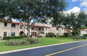 Stucco exterior with red tile roofing, covered entryways, manicured landscaping featuring mature trees