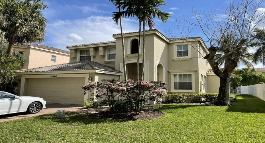Two-story stucco exterior featuring a tiled roof, arched architectural details, a multi-car garage, and established palm trees