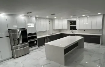 Kitchen featuring high-gloss white upper cabinetry, dark lower cabinetry, a large central island with a stone-finish waterfall countertop, stainless steel appliances, and large-format tile flooring