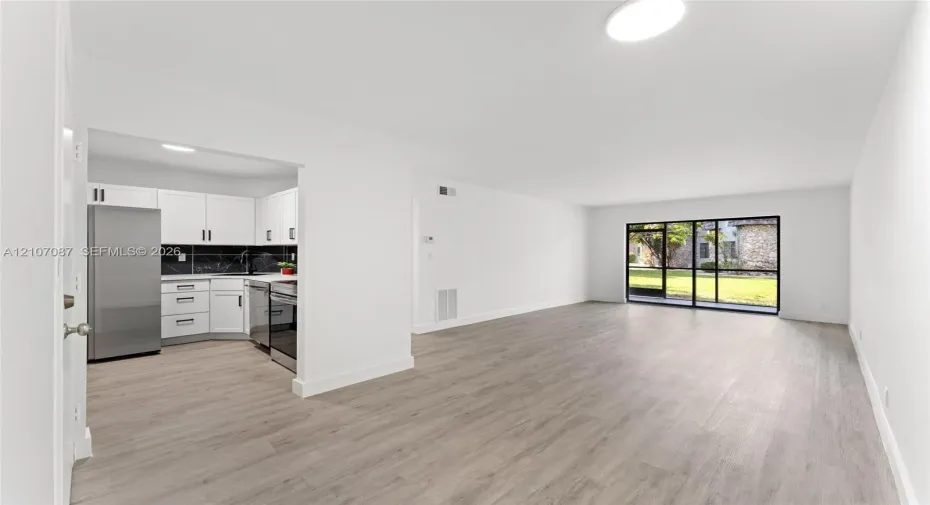 Kitchen featuring white shaker cabinetry, stainless steel appliances, and dark tile backsplash, complemented by wood-finish flooring and floor-to-ceiling glass sliding doors