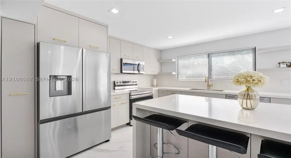 Kitchen featuring flat-panel cabinetry with gold-tone hardware, a central island with a solid-surface countertop, stainless steel appliances, and recessed lighting