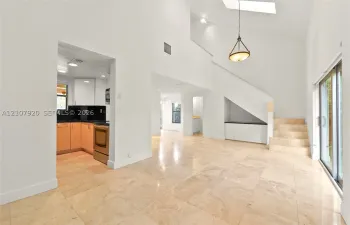 Open-concept living space featuring high vaulted ceilings, large skylight, natural stone flooring, custom built-in cabinetry, and sliding glass doors