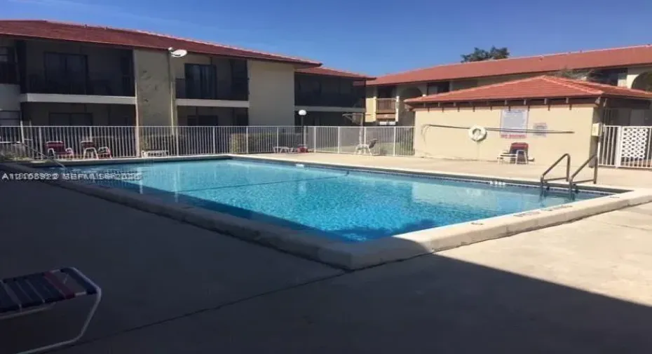 Rectangular swimming pool featuring a concrete deck, perimeter fencing, and metal entry handrails
