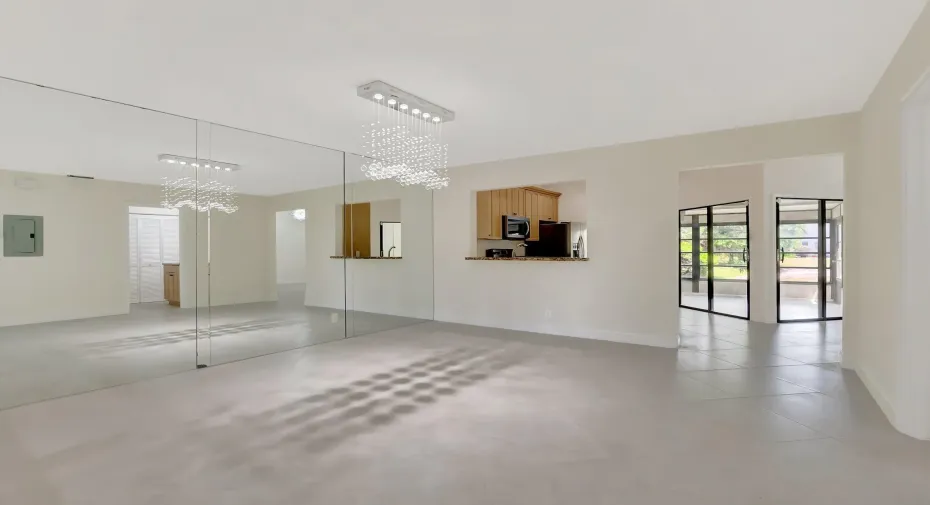 Large-format mirror wall with a crystal-accented chandelier, expansive tile flooring, pass-through kitchen opening, and multi-pane black-frame glass doors