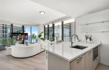 Kitchen featuring a white quartz countertop, undermount sink, gooseneck faucet, light-finish cabinetry, and built-in microwave, complemented by wood-finish flooring and floor-to-ceiling windows