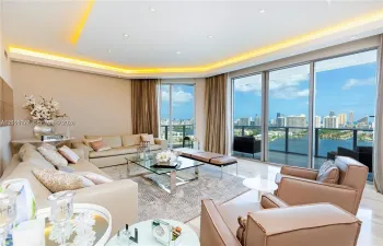Floor-to-ceiling glass sliding doors, recessed tray ceiling with integrated cove lighting, polished neutral-toned flooring, and expansive panoramic water and cityscape horizon