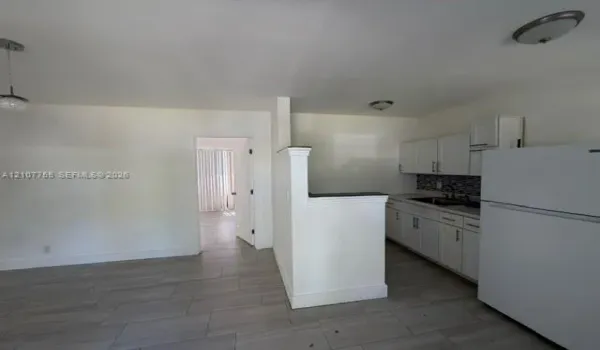 Kitchen featuring white shaker-style cabinetry, a decorative mosaic tile backsplash, solid-surface countertops, and wood-finish tile flooring throughout