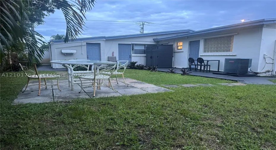 Rear exterior featuring a concrete paver patio, established lawn, and multiple entry points
