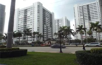 Multi-story high-rise architecture featuring white concrete facade, grid-patterned balconies, floor-to-ceiling windows, and surrounding palm tree landscaping