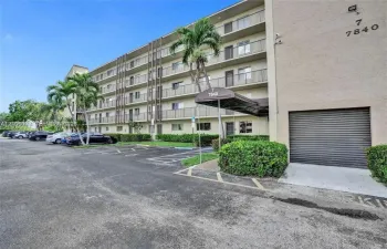 Mid-rise multi-story building exterior featuring stucco cladding, integrated private balconies, a covered entryway, and onsite surface parking