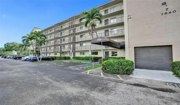 Mid-rise multi-story building exterior featuring stucco cladding, integrated private balconies, a covered entryway, and onsite surface parking