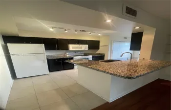 Kitchen featuring dark cabinetry, stone-surface countertops, tile flooring, a peninsula breakfast bar, and stainless steel undermount sink