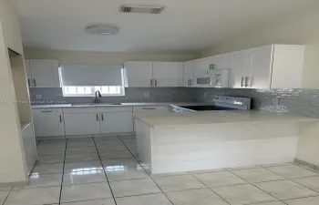 Kitchen featuring white shaker-style cabinetry, light-toned stone countertops, a mosaic tile backsplash, a peninsula, and tile flooring