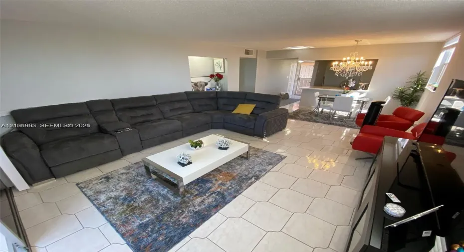 Open-concept interior featuring light-toned tile flooring, recessed ceiling lighting, and a chandelier-style fixture