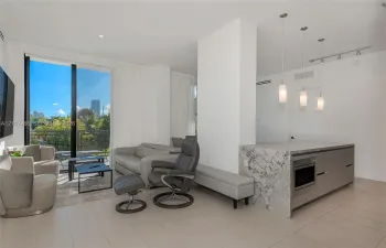 Open-concept floor plan featuring tile flooring, stone-surfaced kitchen island with integrated cabinetry, floor-to-ceiling glass paneling, and three cylindrical pendant light fixtures
