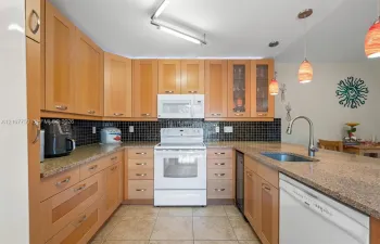 Kitchen featuring light-finish wood cabinetry, speckled stone countertops, a black tile backsplash, integrated stainless steel appliances, and a central island with a built-in beverage refrigerator