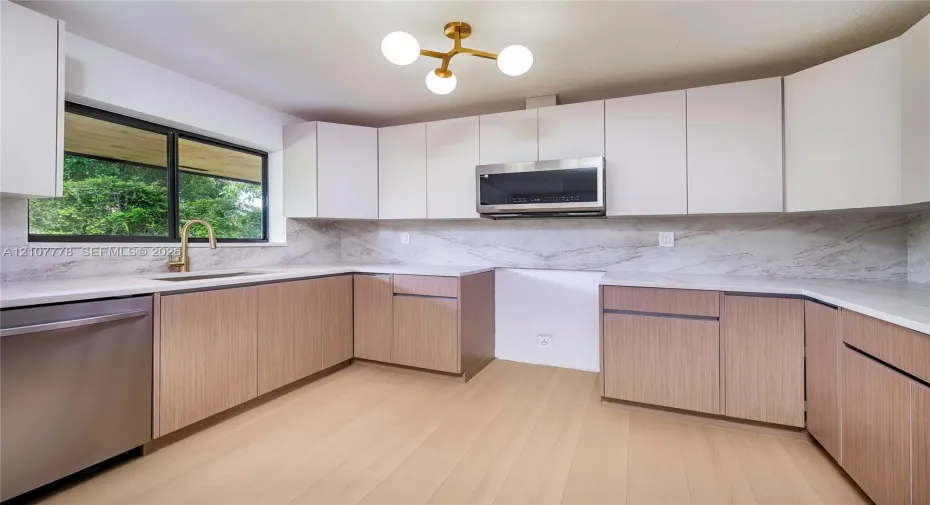 Kitchen featuring flat-panel wood-finish lower cabinetry, white upper cabinetry, stone-look backsplash, stainless steel appliances, and a modern gold-tone multi-arm chandelier