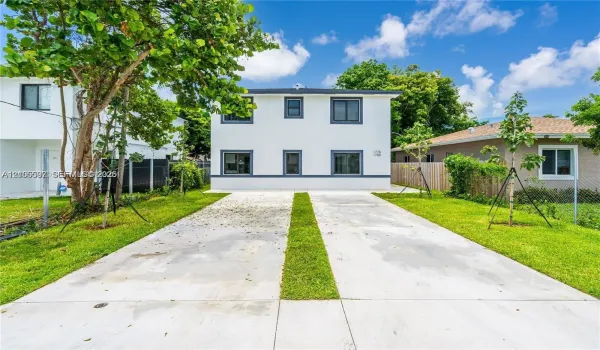 Two-story exterior featuring a smooth stucco finish, multi-pane windows with dark trim, and a concrete driveway with a central grass inlay